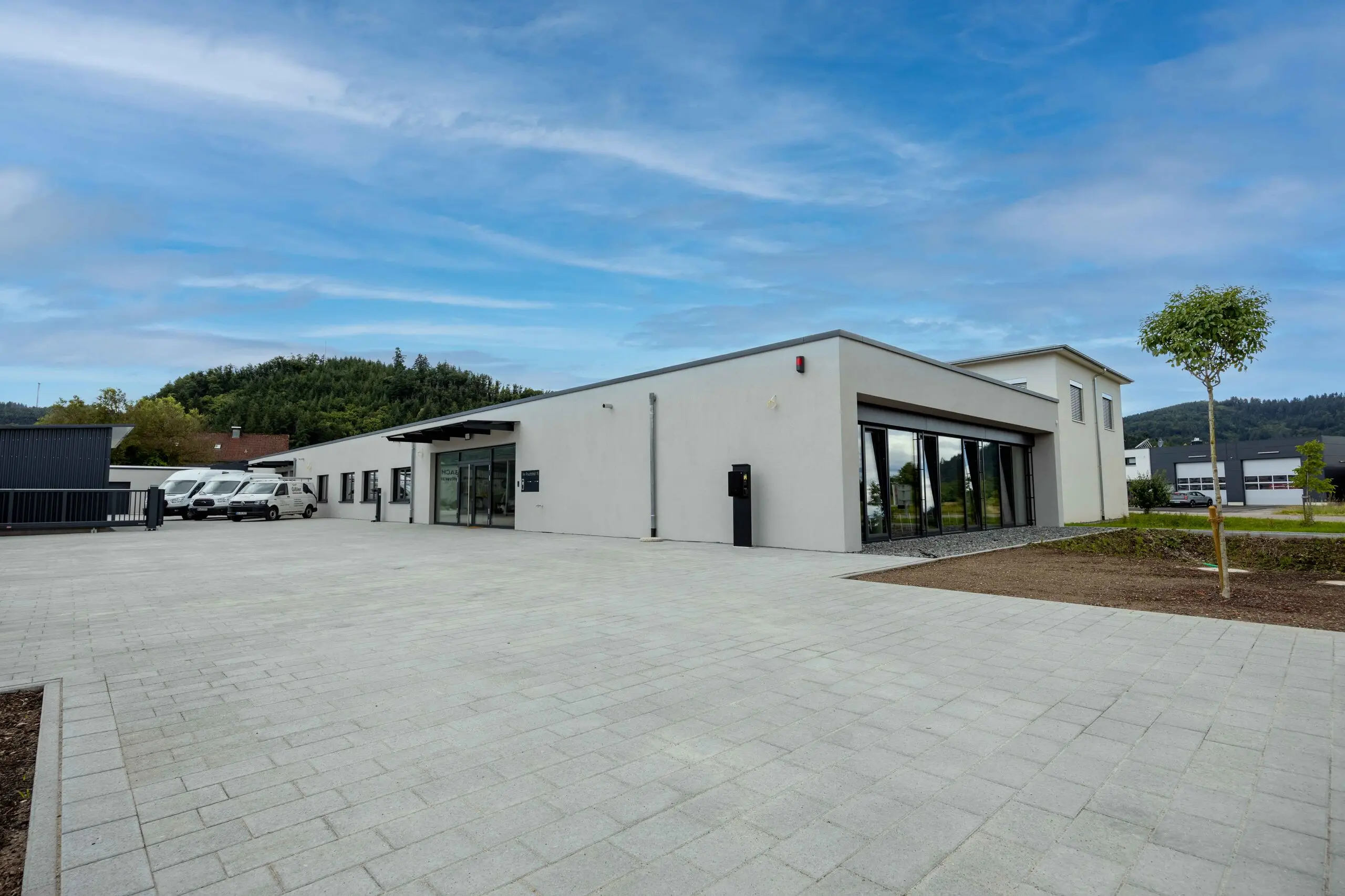 Firmengebäude der SEB-Solar in Berghaupten mit gepflastertem Vorplatz, Firmenfahrzeugen und bewaldeten Hügeln im Hintergrund