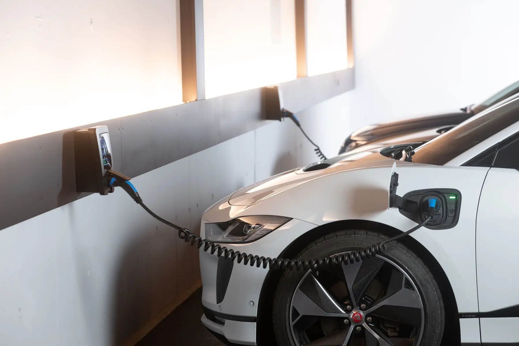 Weißes Elektroauto lädt an einer Wallbox in einer Garage, dahinter ein zweites Auto an einer weiteren Wallbox