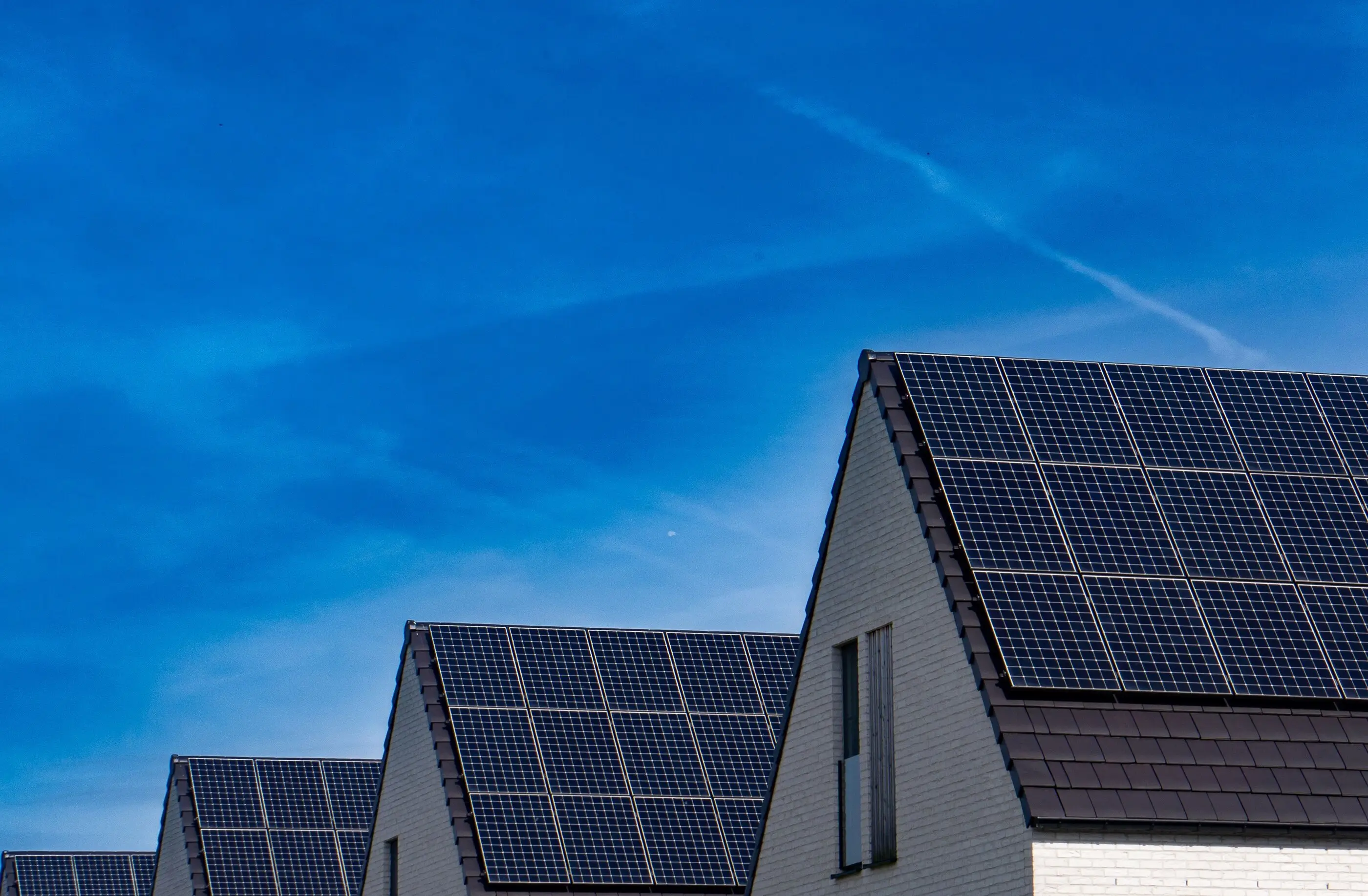 Wohnhäuser mit schwarzen Solarmodulen auf den Satteldächern vor blauem Himmel