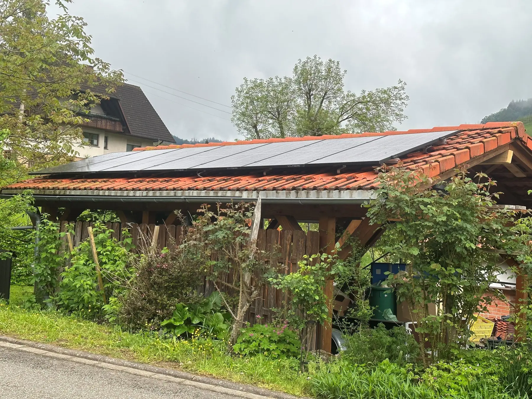 Solarmodule auf dem Ziegeldach eines Holz-Carports, dahinter Wohnhäuser und bewaldete Hänge im Kinzigtal