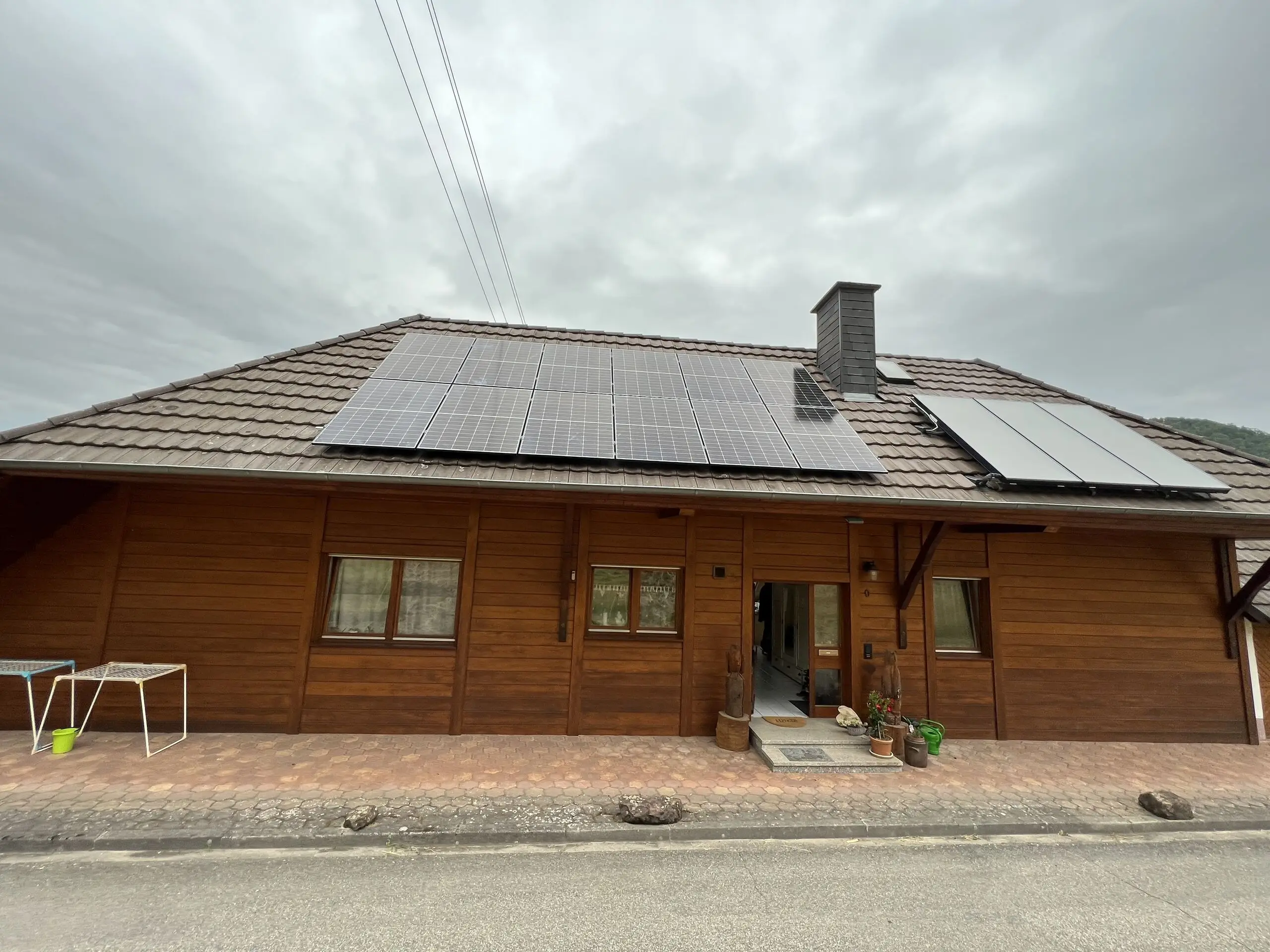 Wohnhaus mit Holzfassade, auf dem Ziegeldach Photovoltaikmodule und daneben Solarthermie-Kollektoren