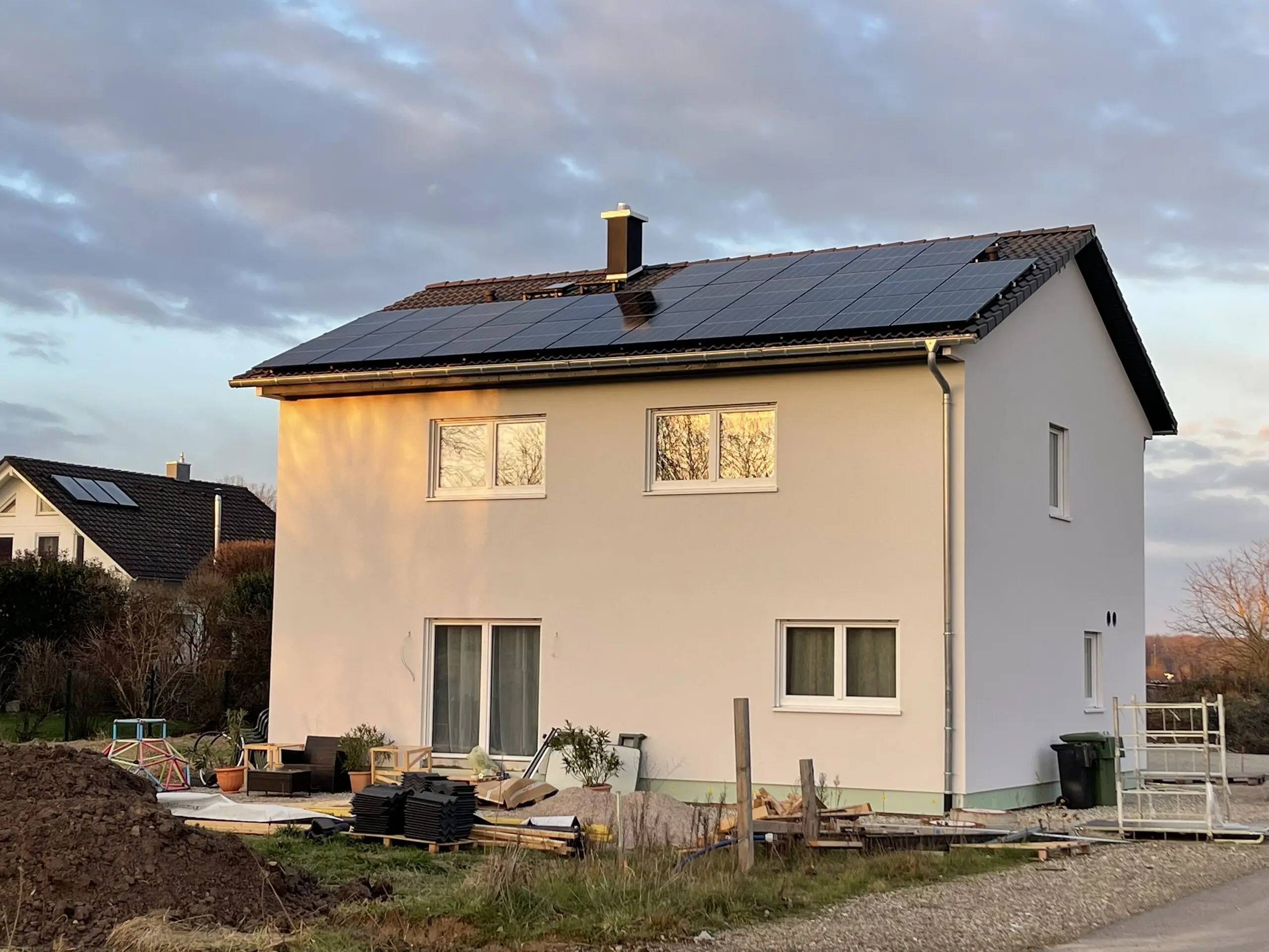 Neu gebautes Einfamilienhaus im Abendlicht, auf dem Satteldach eine Photovoltaikanlage aus schwarzen Modulen