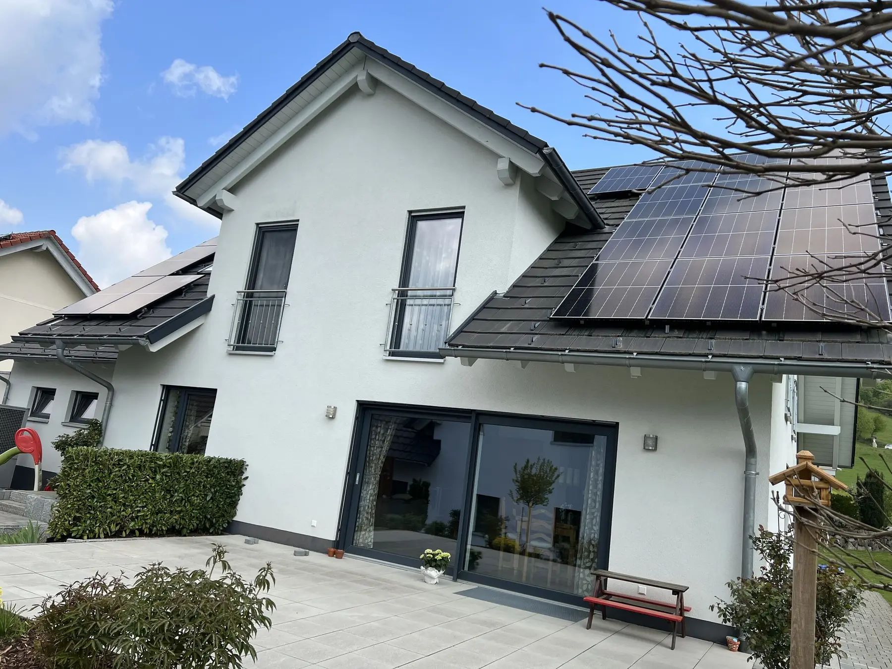 Weißes Einfamilienhaus mit großer Glastür zur Terrasse, auf den dunklen Dachflächen schwarze Solarmodule