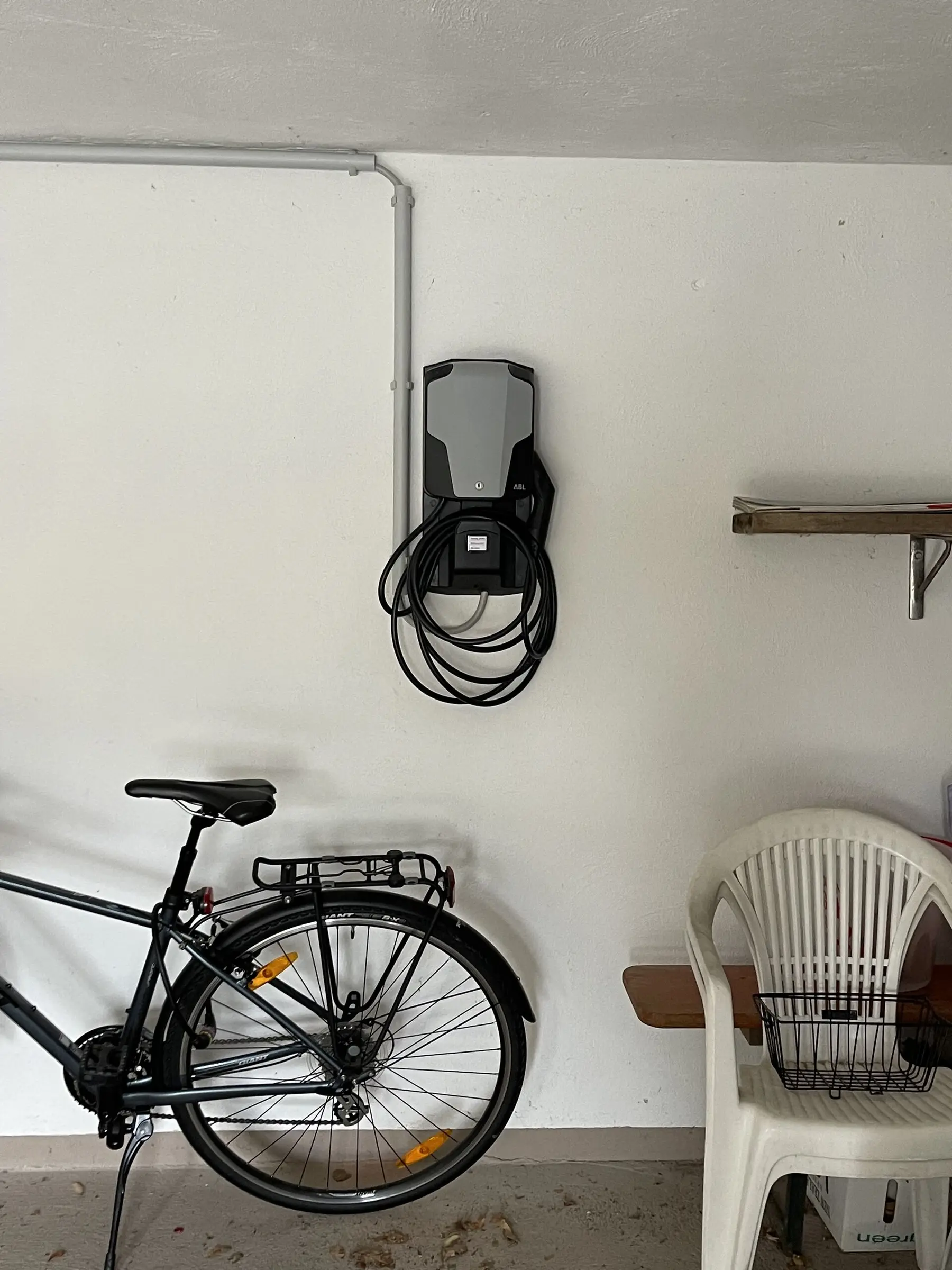 Wallbox mit aufgewickeltem Ladekabel an der weißen Wand einer Garage, darunter ein Fahrrad