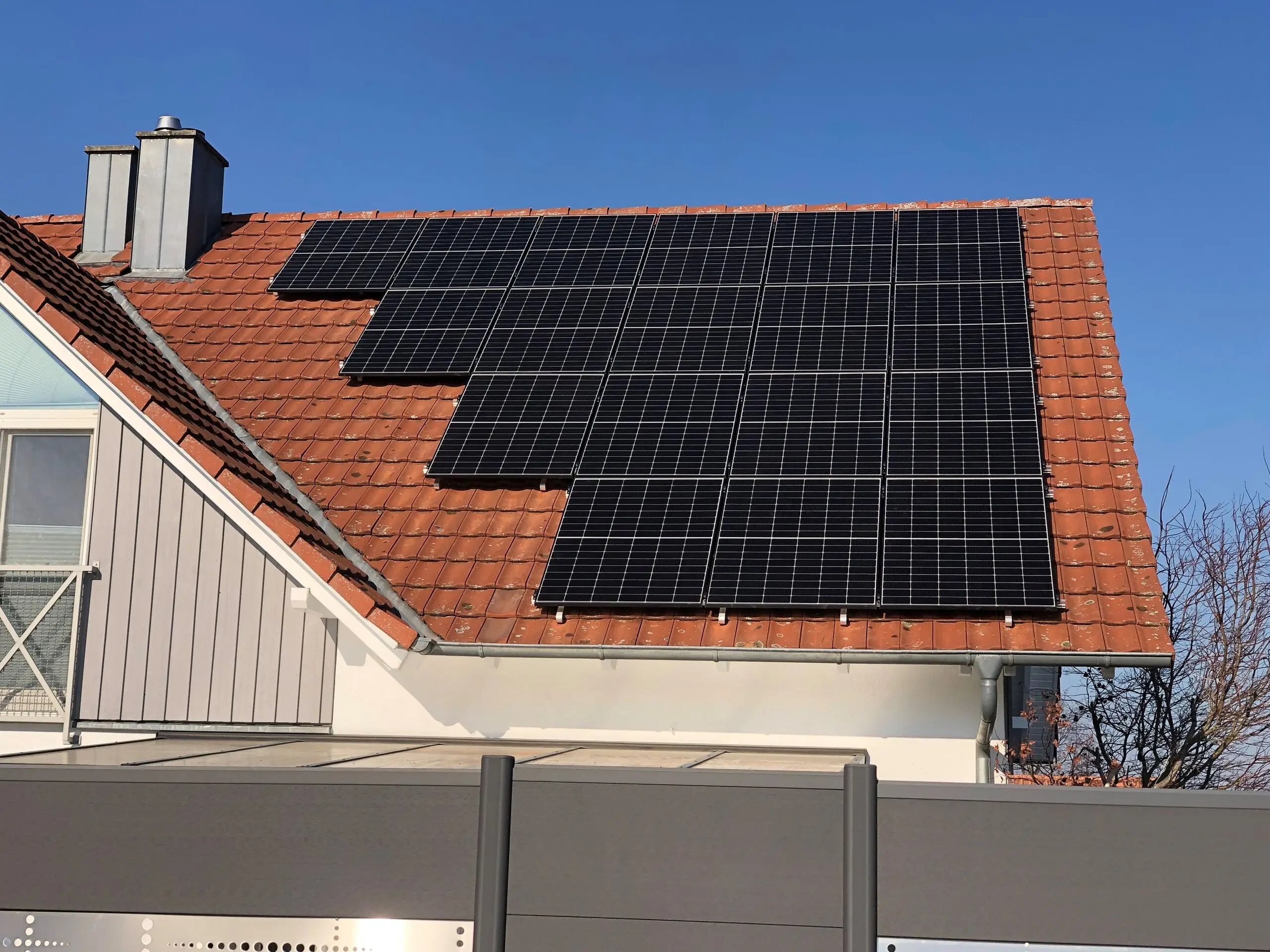 Nachträglich belegtes rotes Ziegeldach: schwarze Photovoltaikmodule in versetzten Reihen um Kamin und Dachfenster herum