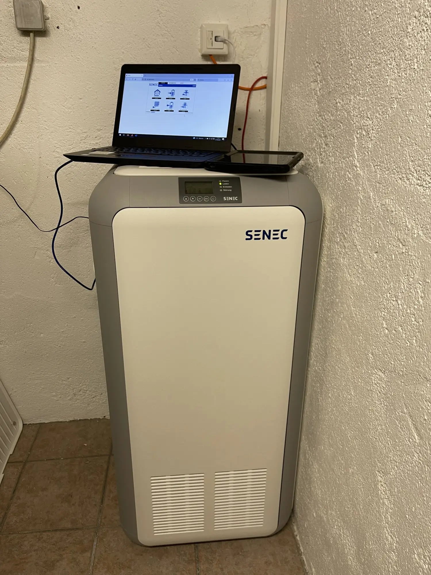 SENEC-Stromspeicher in einem Kellerraum, auf dem Gerät steht ein aufgeklappter Laptop