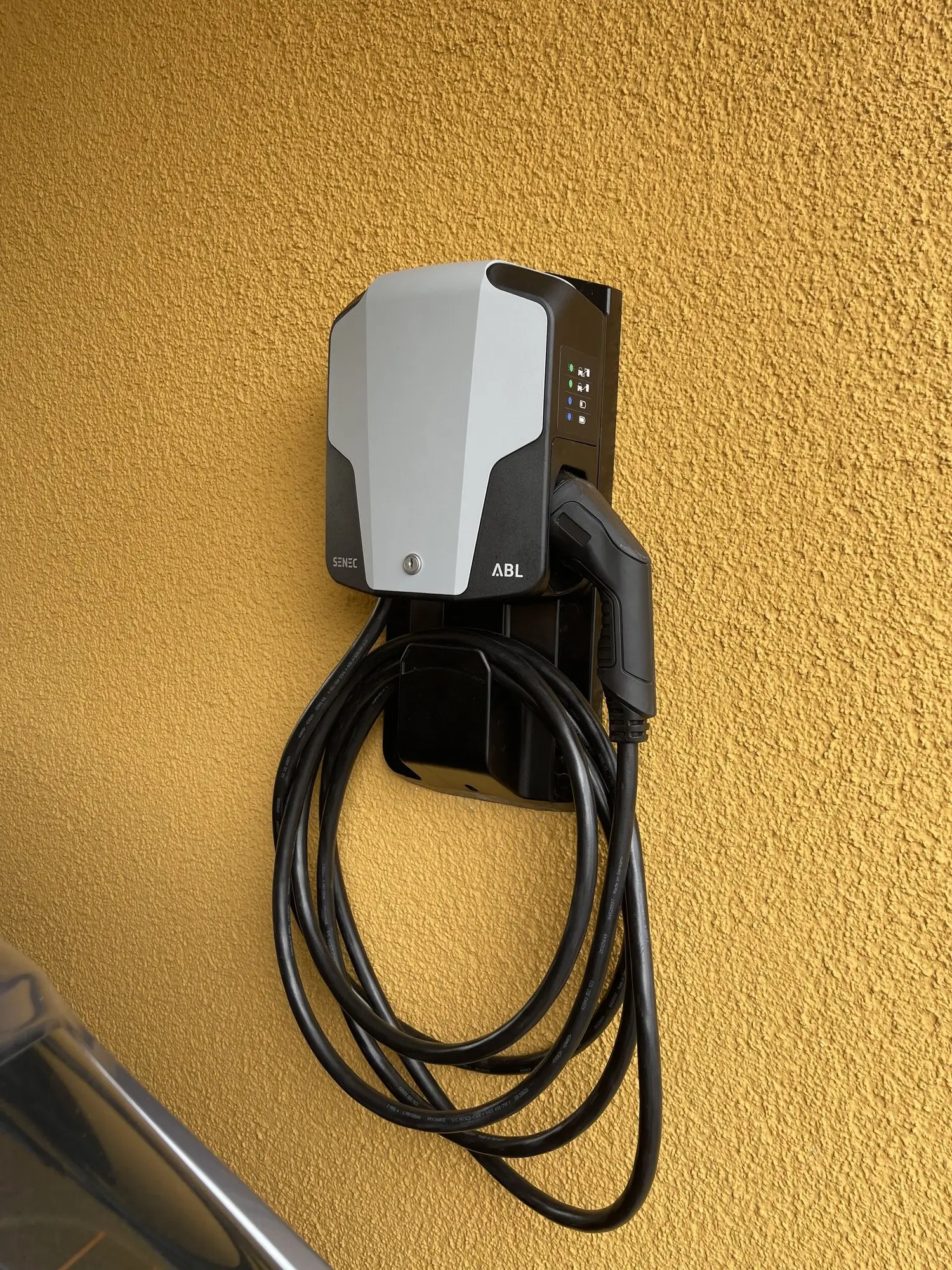 Wallbox mit aufgewickeltem Ladekabel an einer gelb verputzten Hauswand